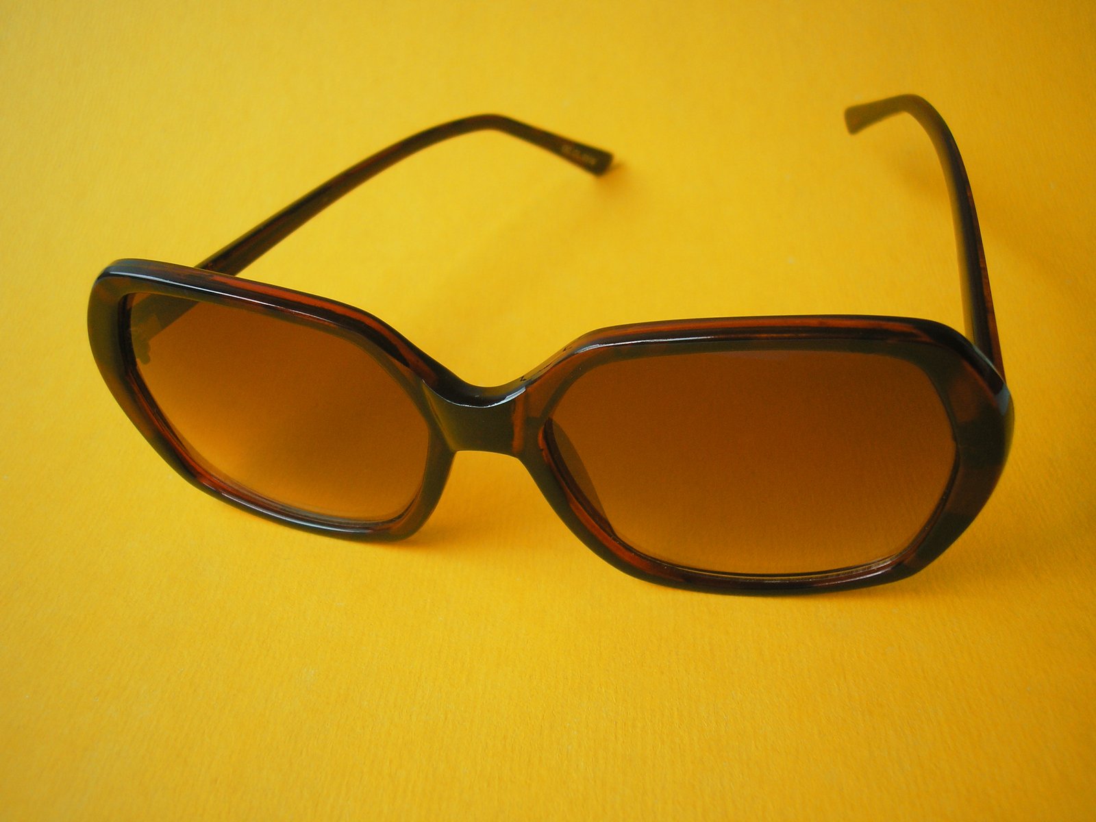 a pair of brown sunglasses on top of a yellow surface
