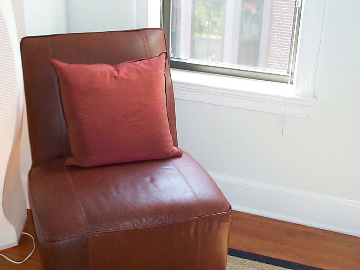 the couch is next to a window with a red cushion on it