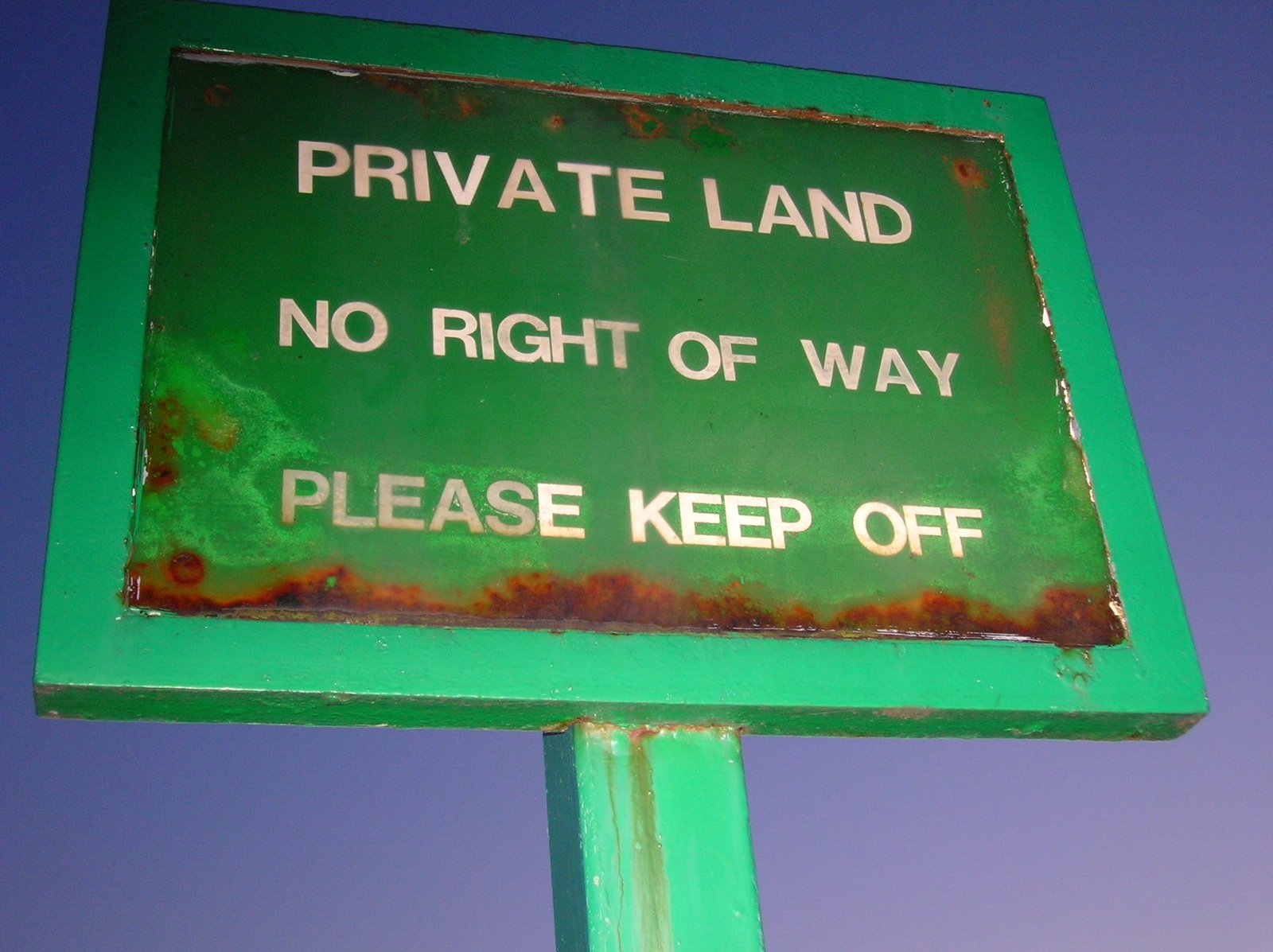 a green sign saying private land is on a street pole