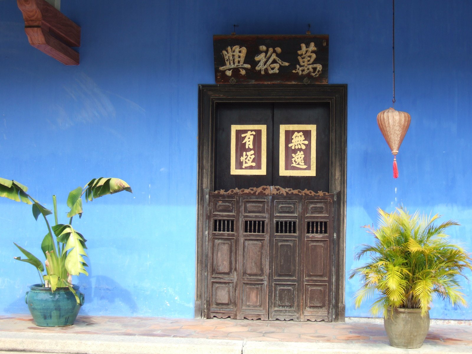 an oriental entrance is painted blue with two flowers in front of it