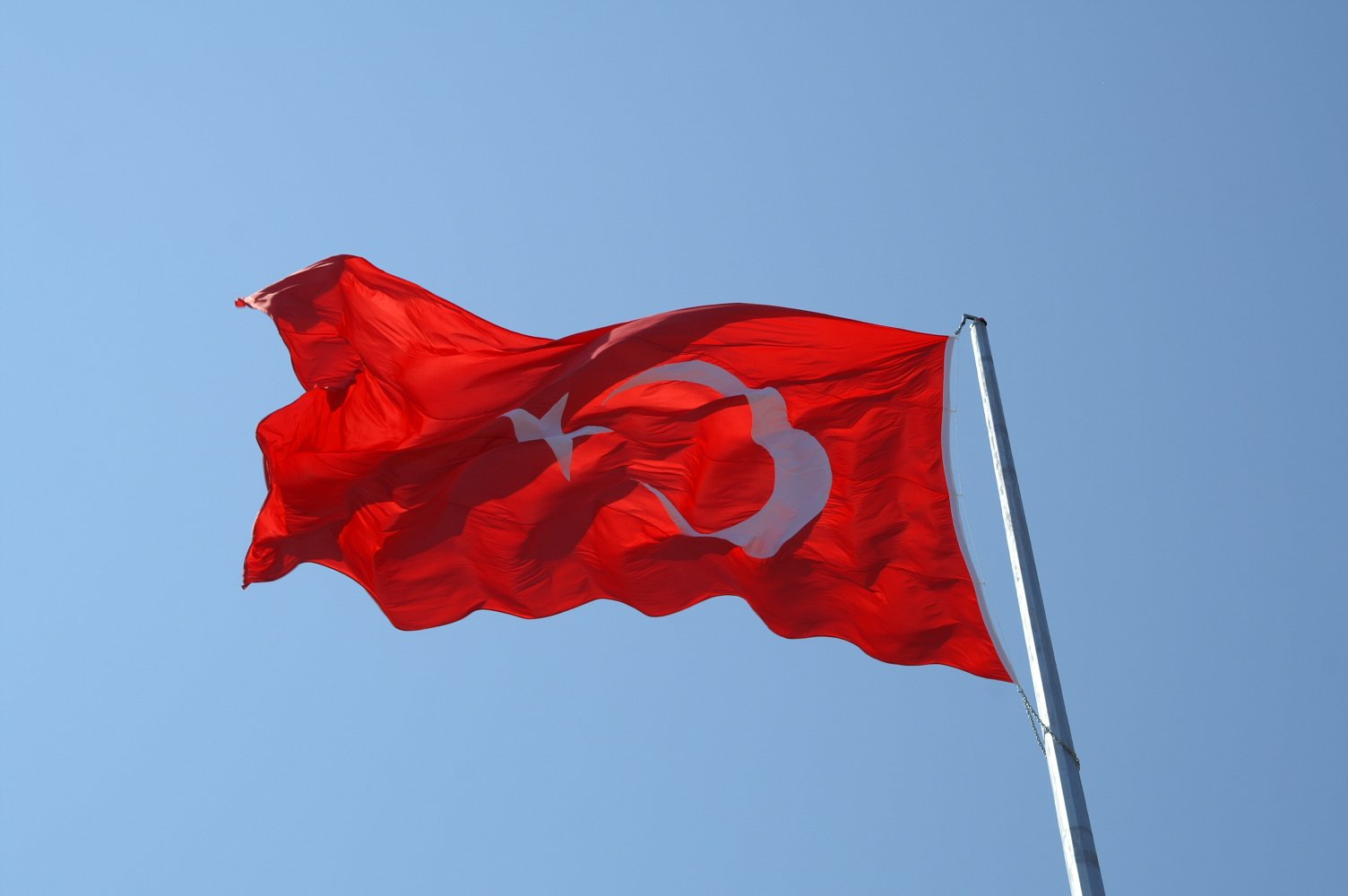 a red flag flying on top of a pole in the blue sky
