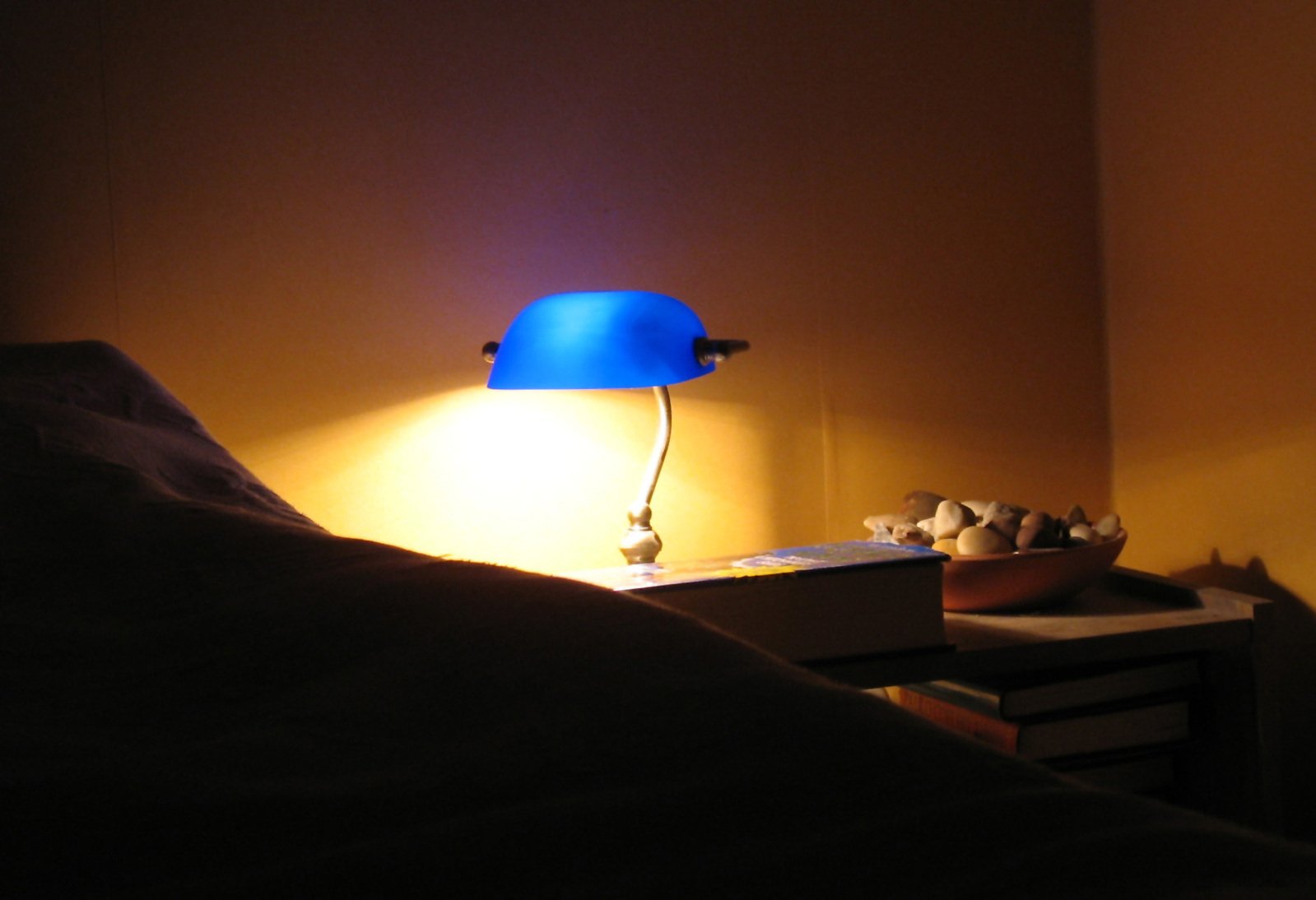 a blue lamp next to a bed with two lamps on
