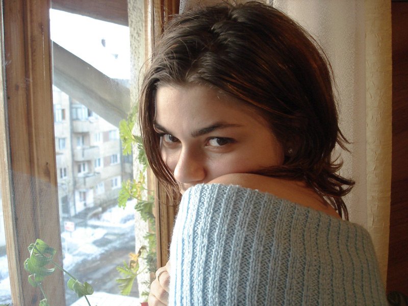 the young woman is posing by the window and looking into the camera