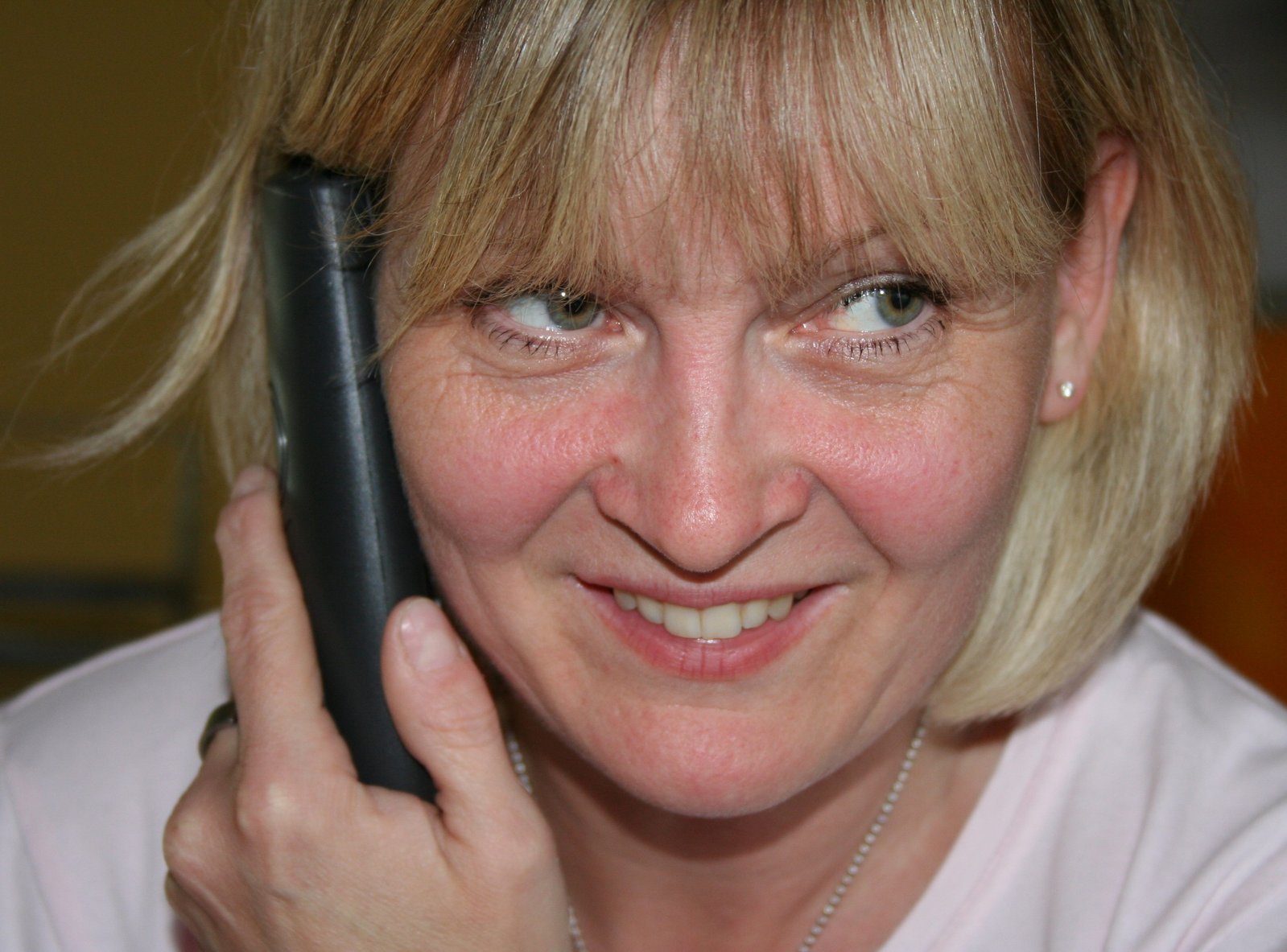 a blond woman smiles at the camera while on her phone