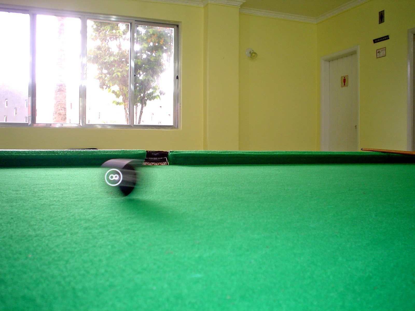 a pool table with a green cloth next to two windows