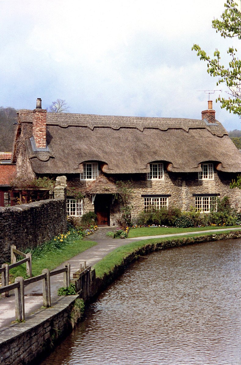 a stone house with thatched roof over the water