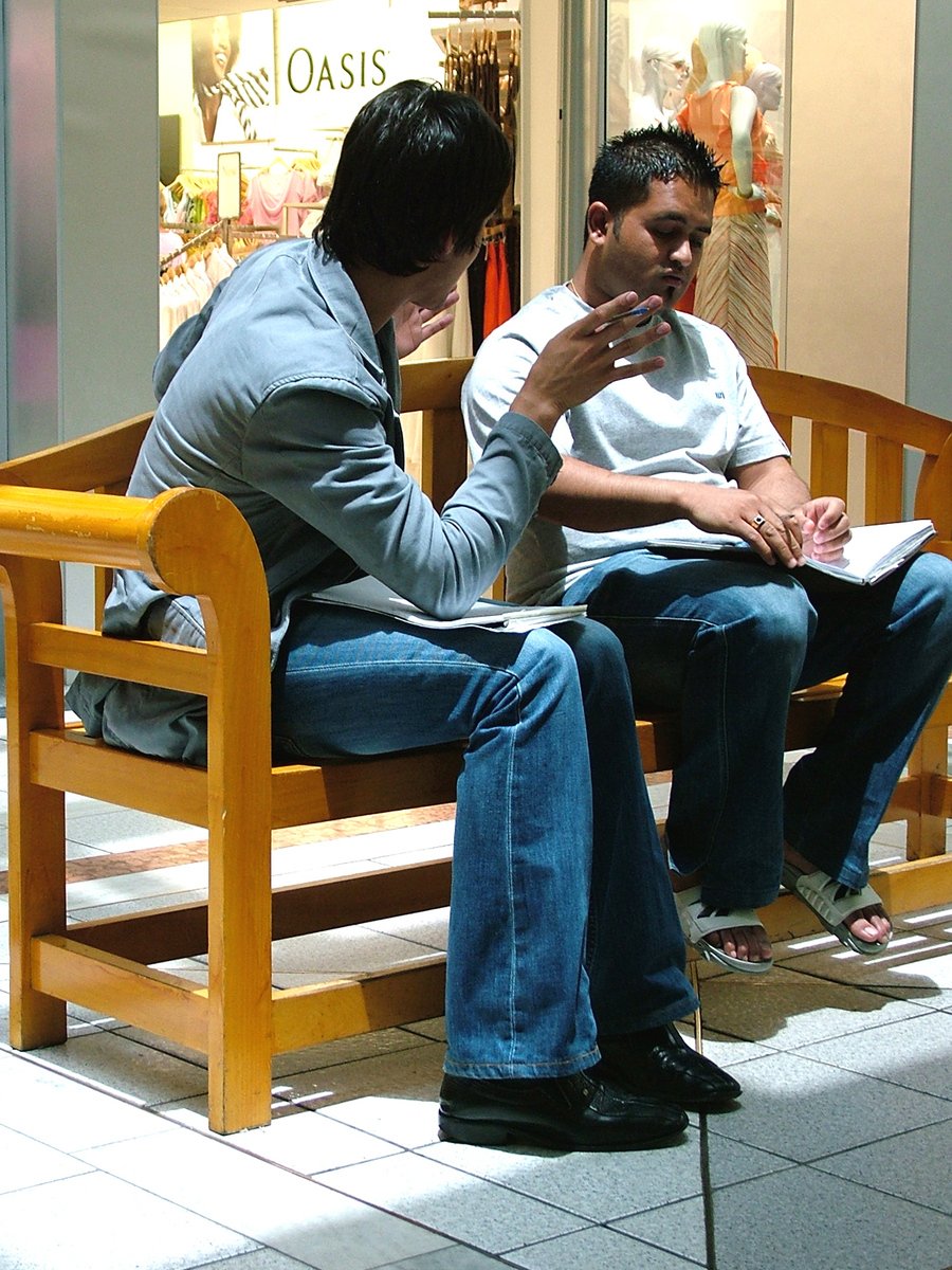 two men sitting on a wooden bench looking at papers