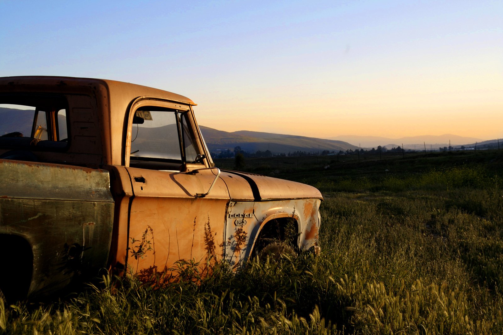 a rusted out truck sits in a field during the sunset