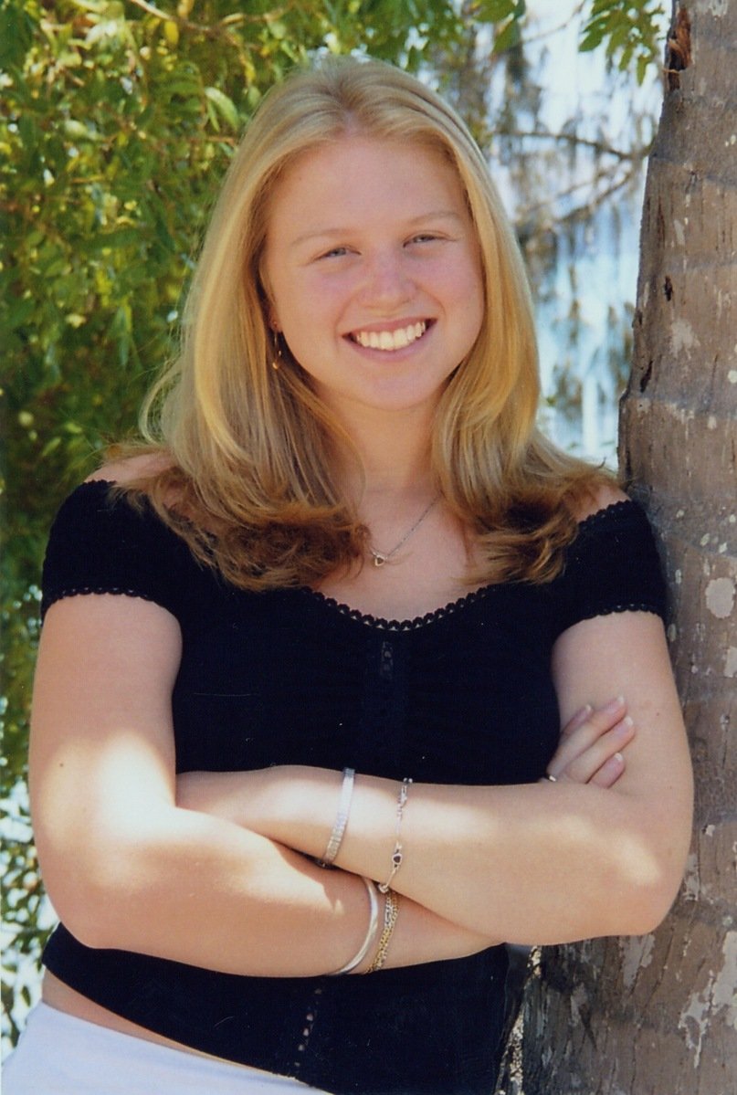 a woman leaning against a tree trunk wearing a black shirt