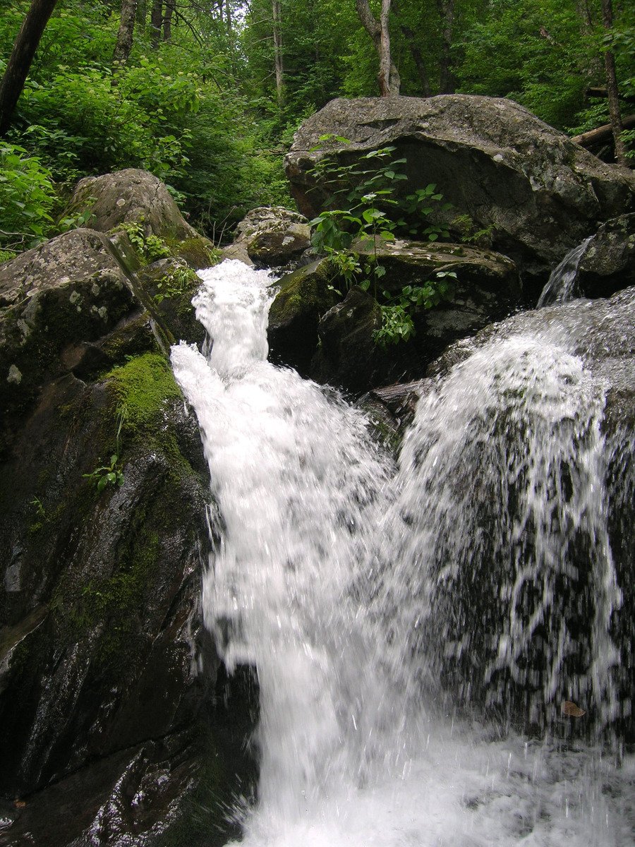 a waterfall is surrounded by big rocks in a forest