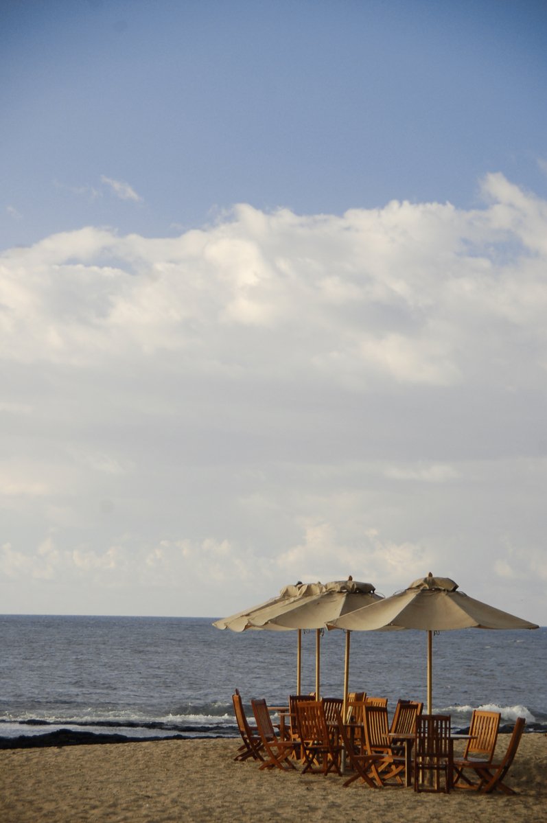 a number of chairs under an umbrella near the ocean