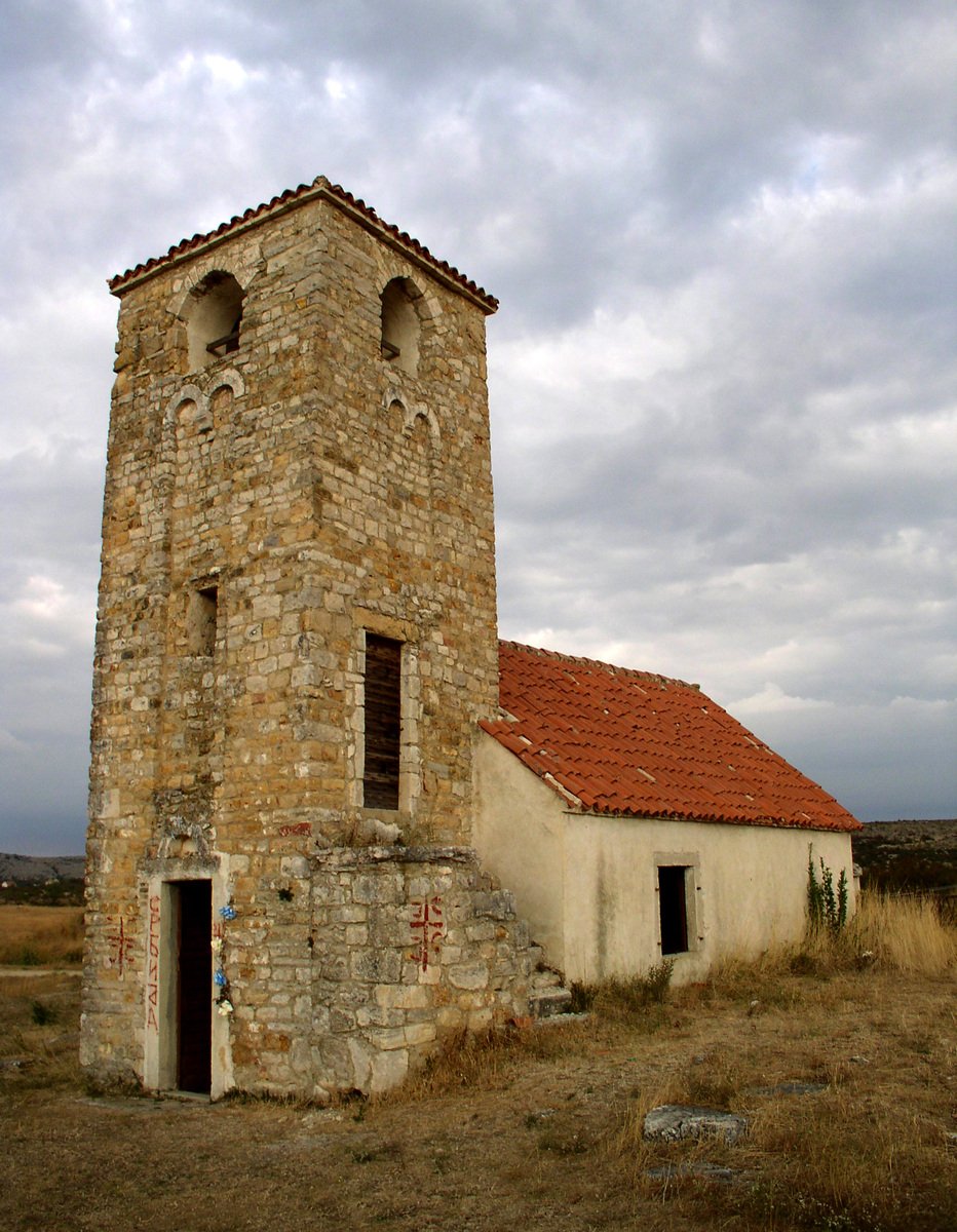 an old adobe church sits alone in a dry grass field