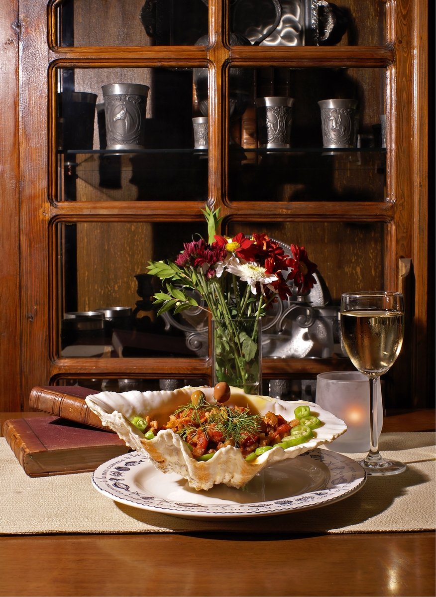 a vase with flowers sits on the table beside a plate of food and wine