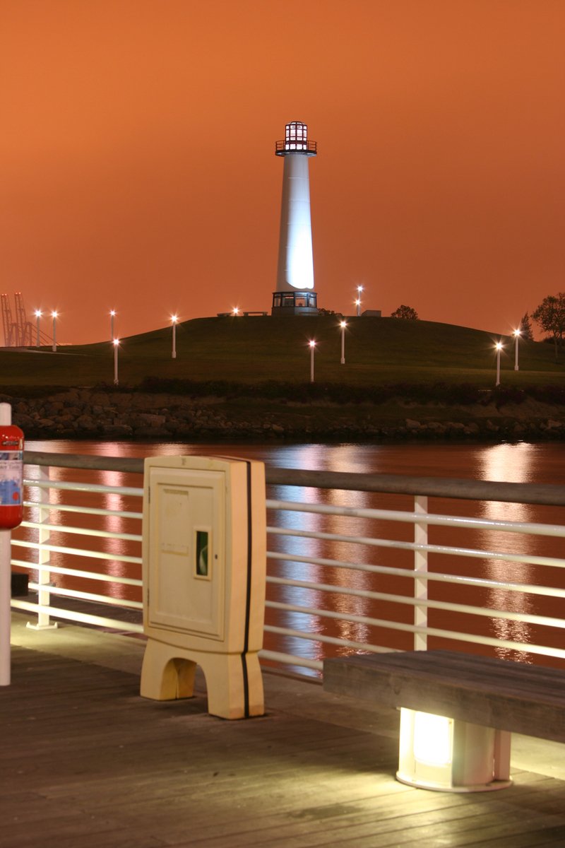 a mail box on the edge of a pier with a light house in the background