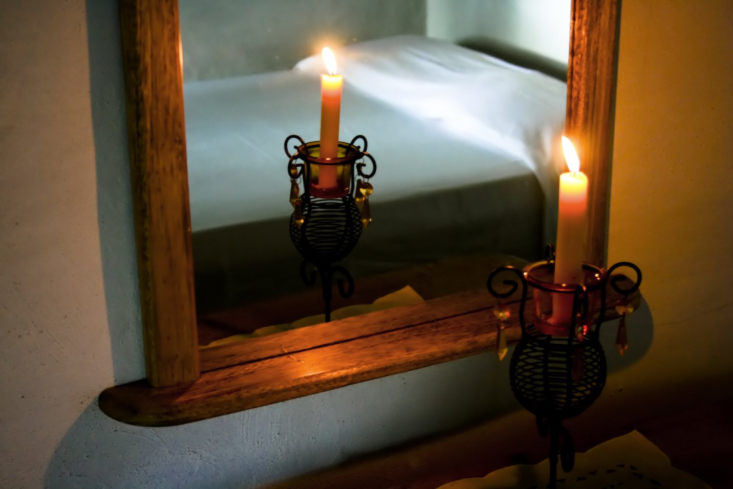 candle lit candles in front of a mirror reflecting a bed