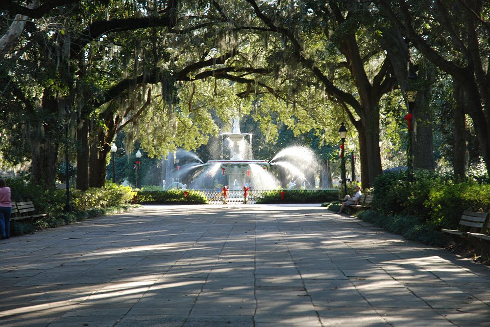 the walkway in the park with people sitting down and facing the fountain