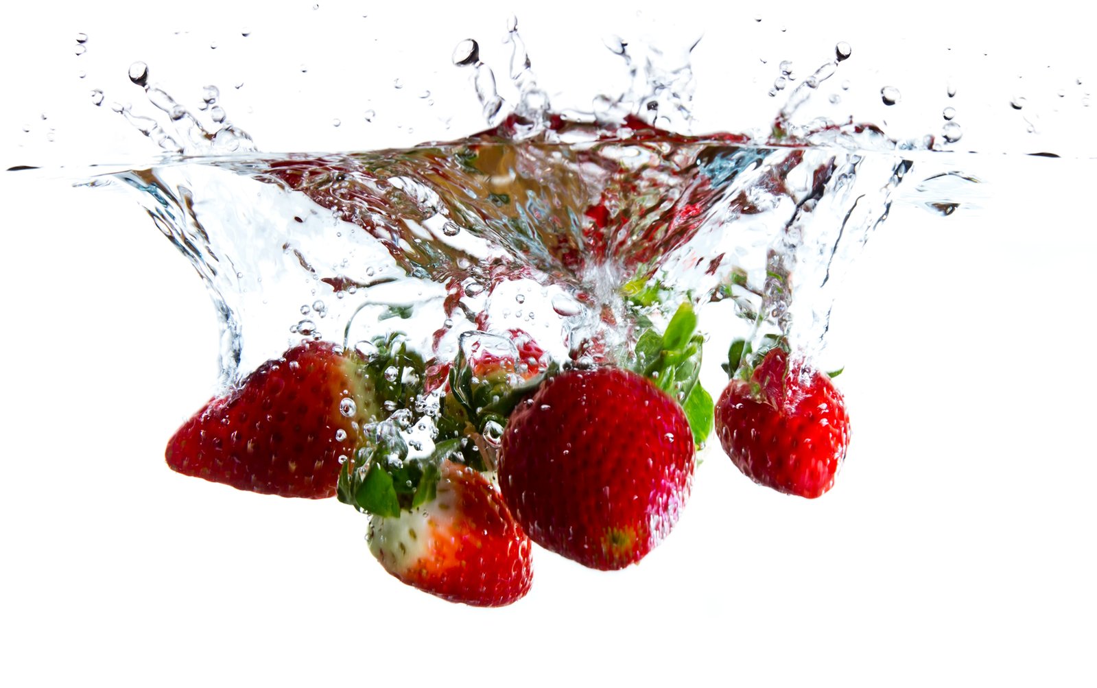 strawberries splashed into water with green leafy stalks