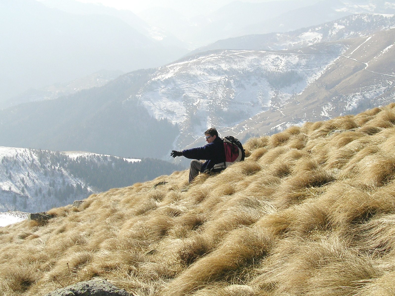 man sitting on top of a grassy hill with mountains in the background