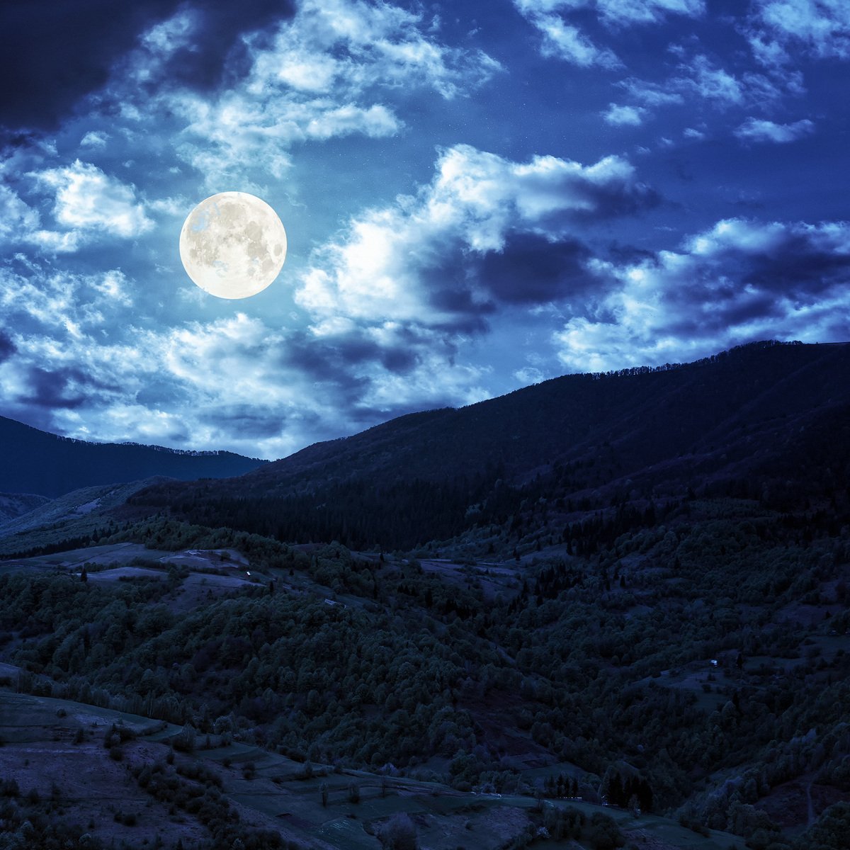 a view of a moon lit mountain with clouds in the background