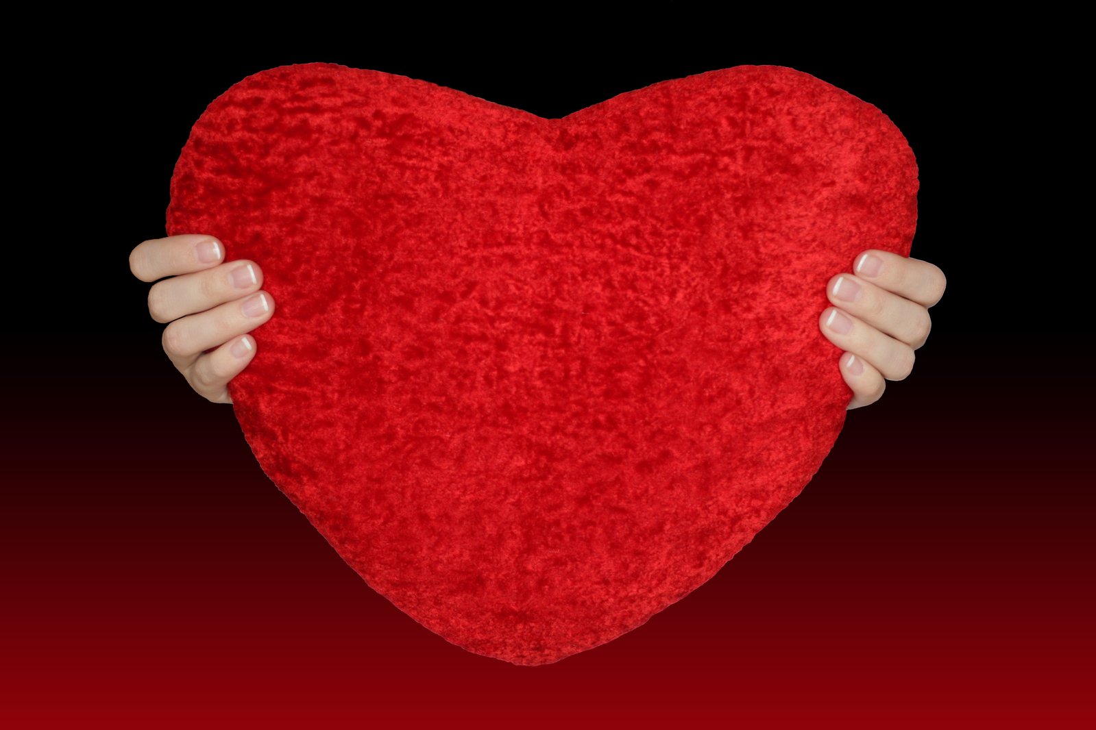 a red heart held up over a black background