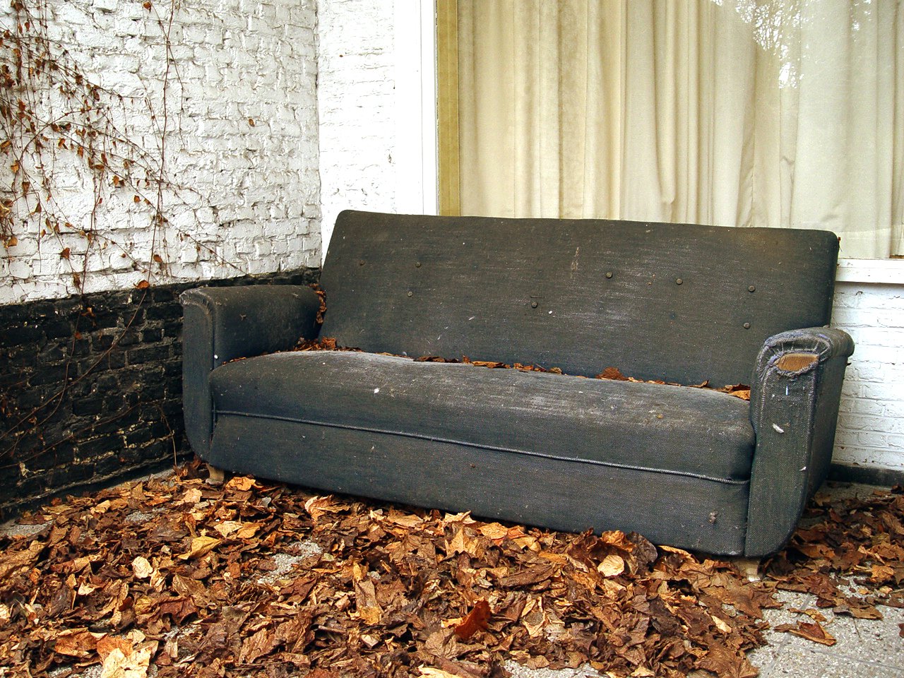 a couch in a pile of dead leaves next to an old building