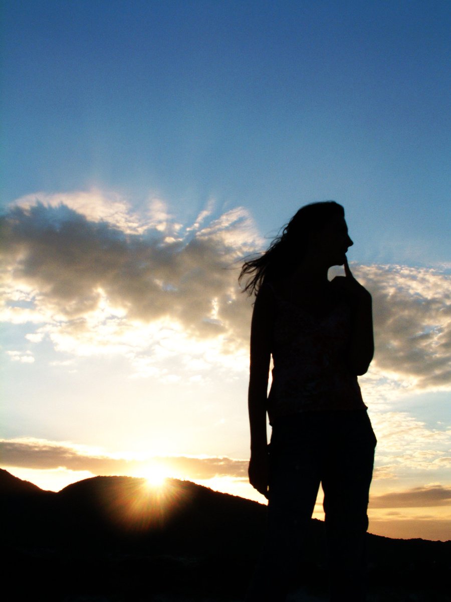 a person standing on the side of a hill with the sun in the distance