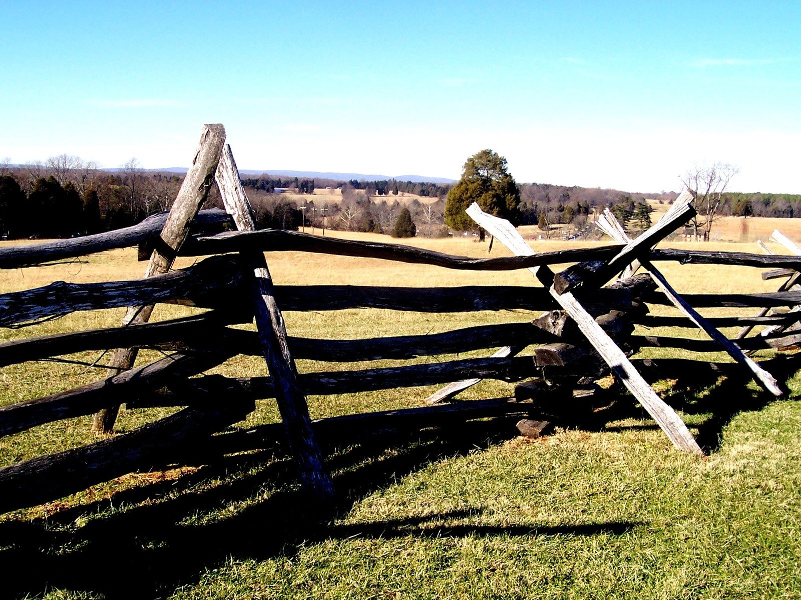 a split wood fence with grass and trees