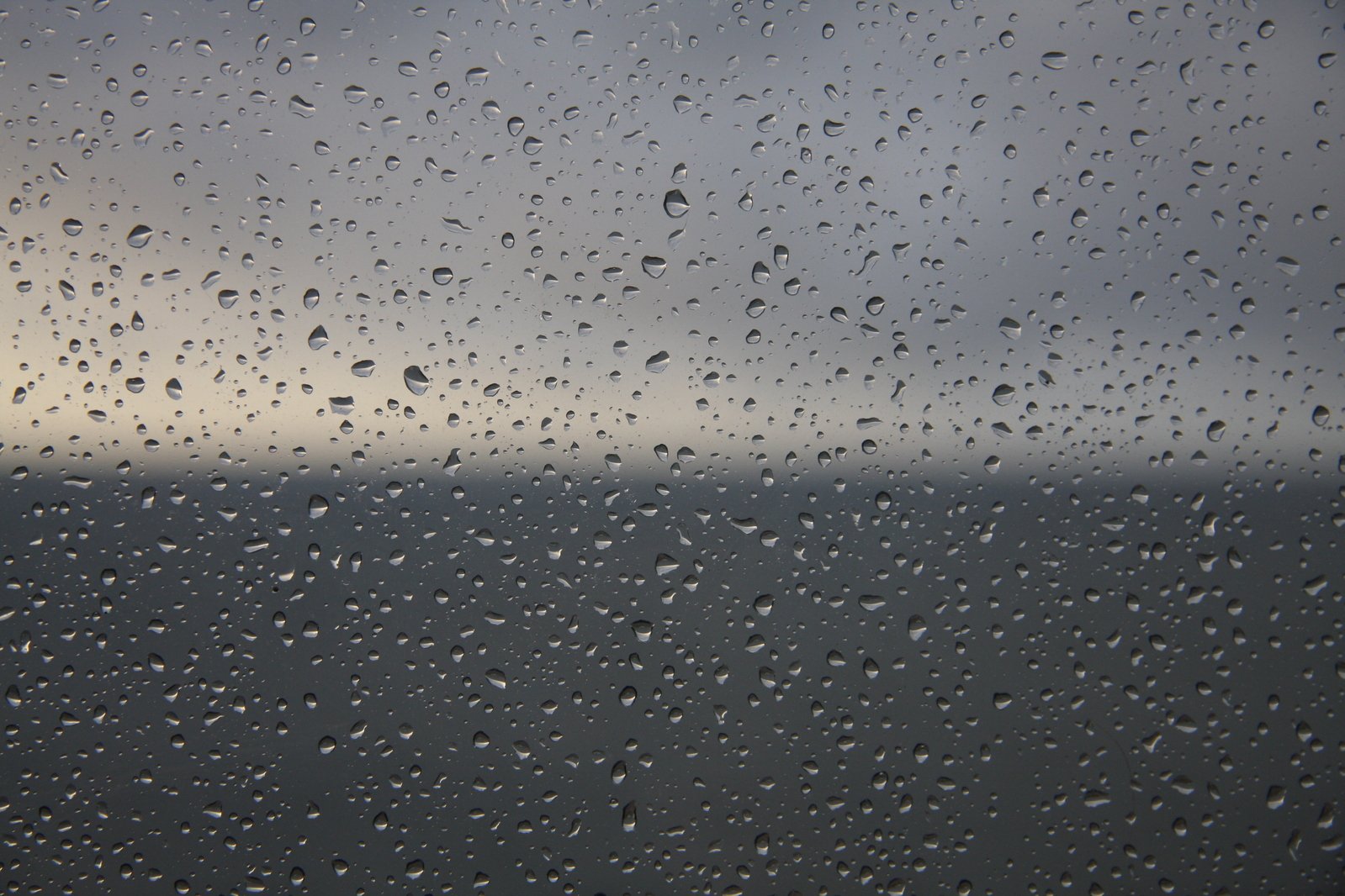 a window with water on the glass with sky and clouds in the background