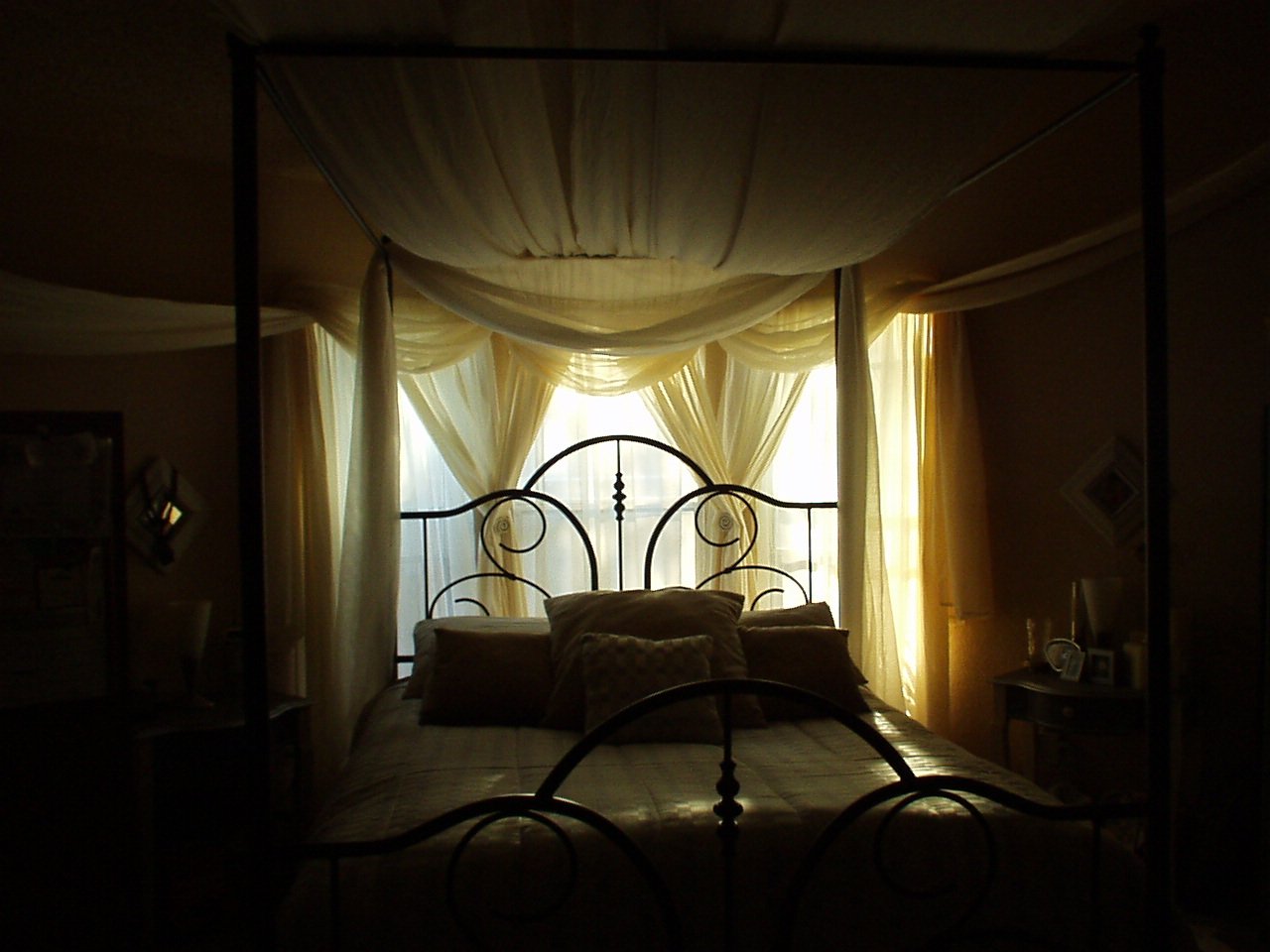 a room with four poster bed and light shining through the curtains