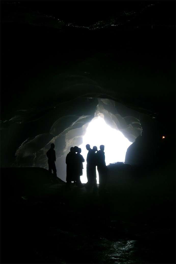 group of people standing inside of a cave with bright light shining through