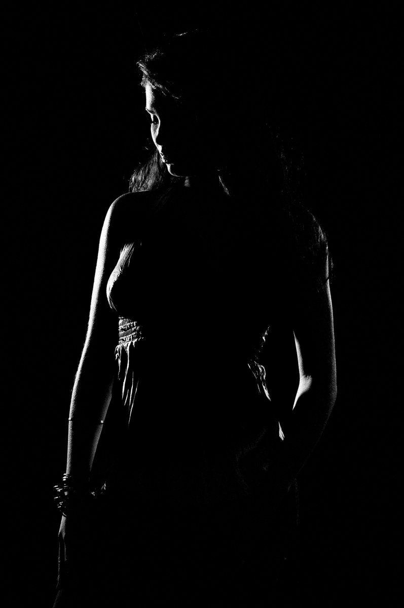 a woman standing in the dark with her arms wrapped around her waist
