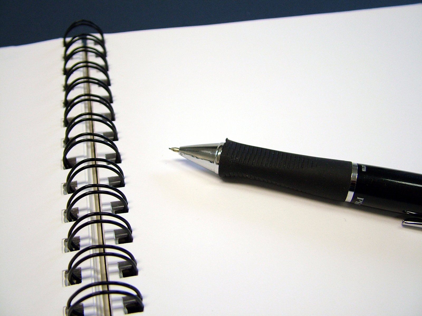 a pen sitting next to a notebook on top of a white desk