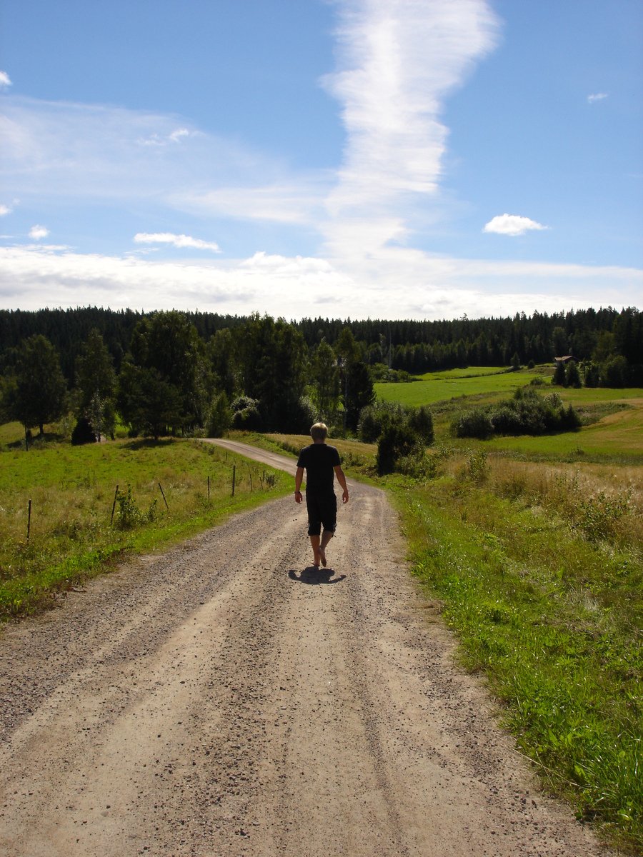 a man walking down a dirt road toward a field