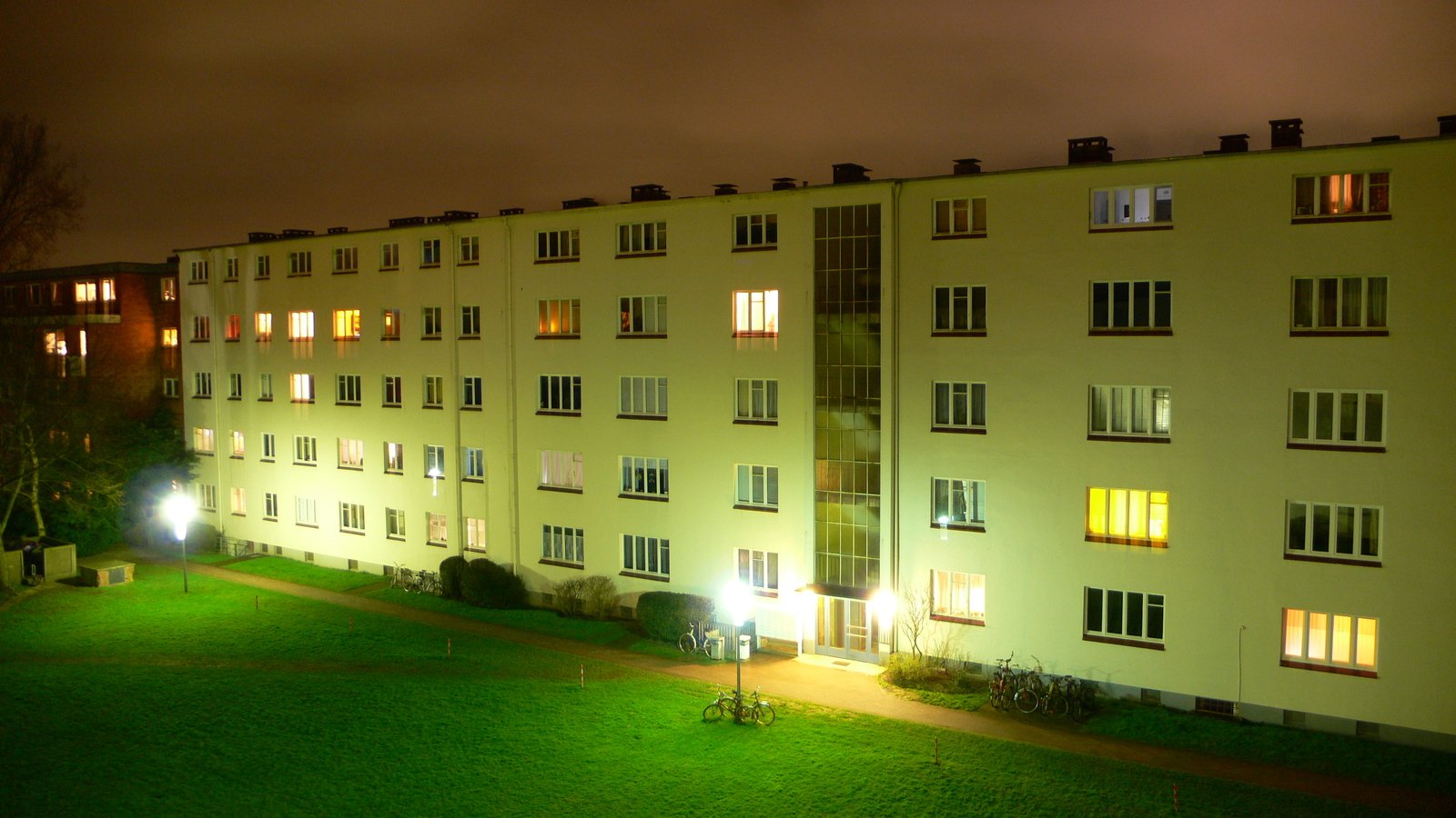 a lawn area with a building and a clock at night