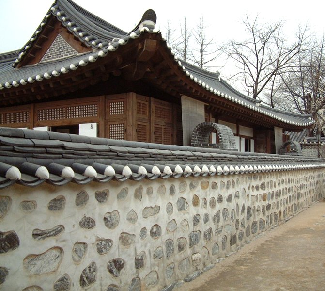 a stone wall near an old building with wooden roof and small round windows