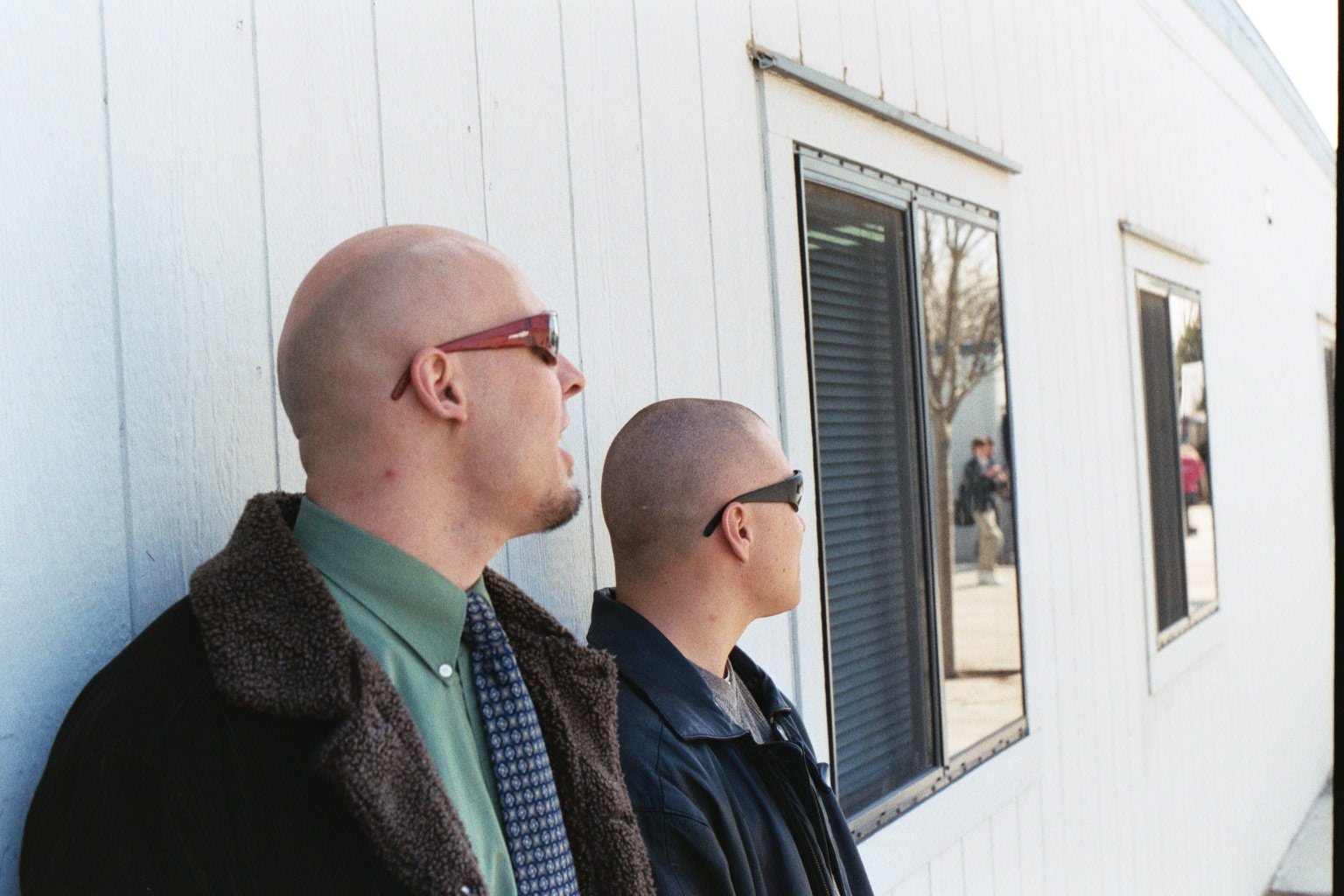 two bald guys standing in front of the window