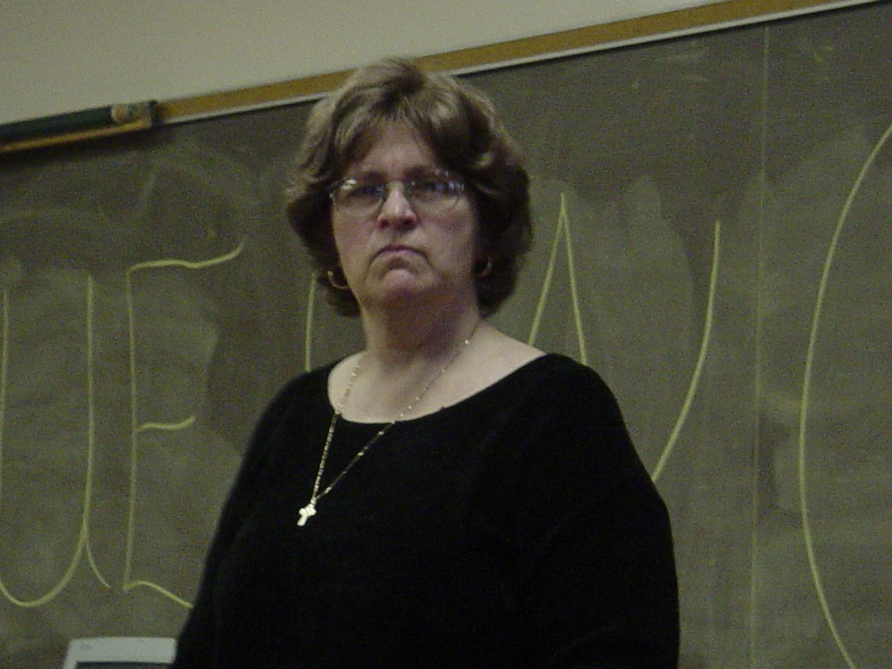 a woman in glasses standing in front of a blackboard with a chalk written on it