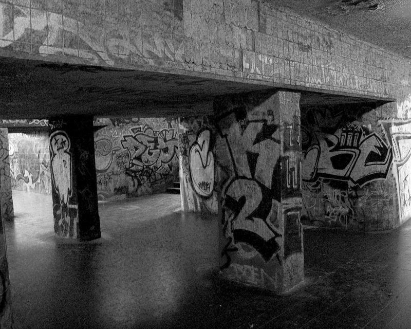 a skateboarder skating under an overpass with graffiti on it