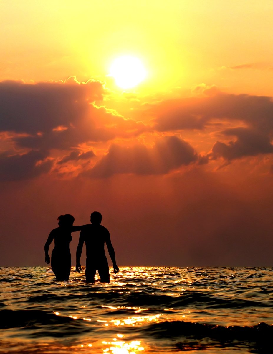 two people on a surf board in the water with a setting sun