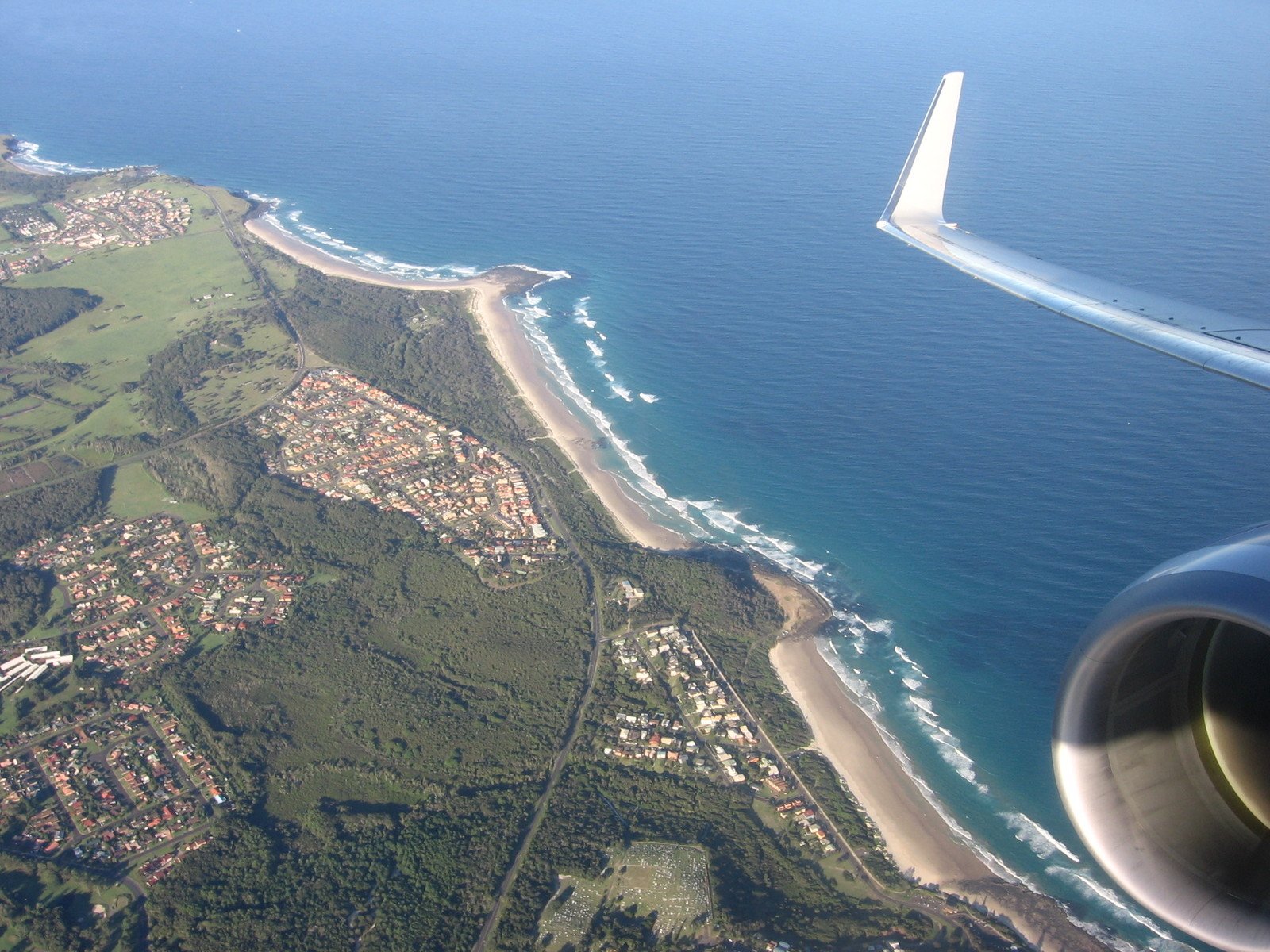 an airplane wing flying over the ocean and land