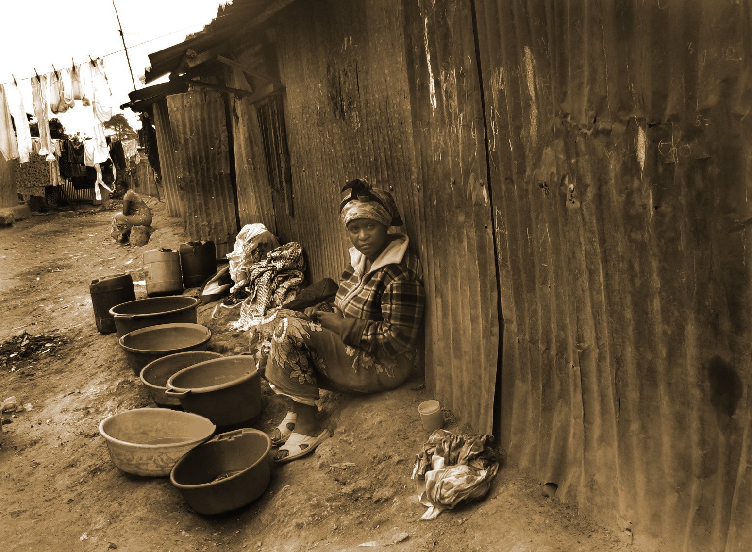 two women sit outside of a mud building, one of them is taking a nap