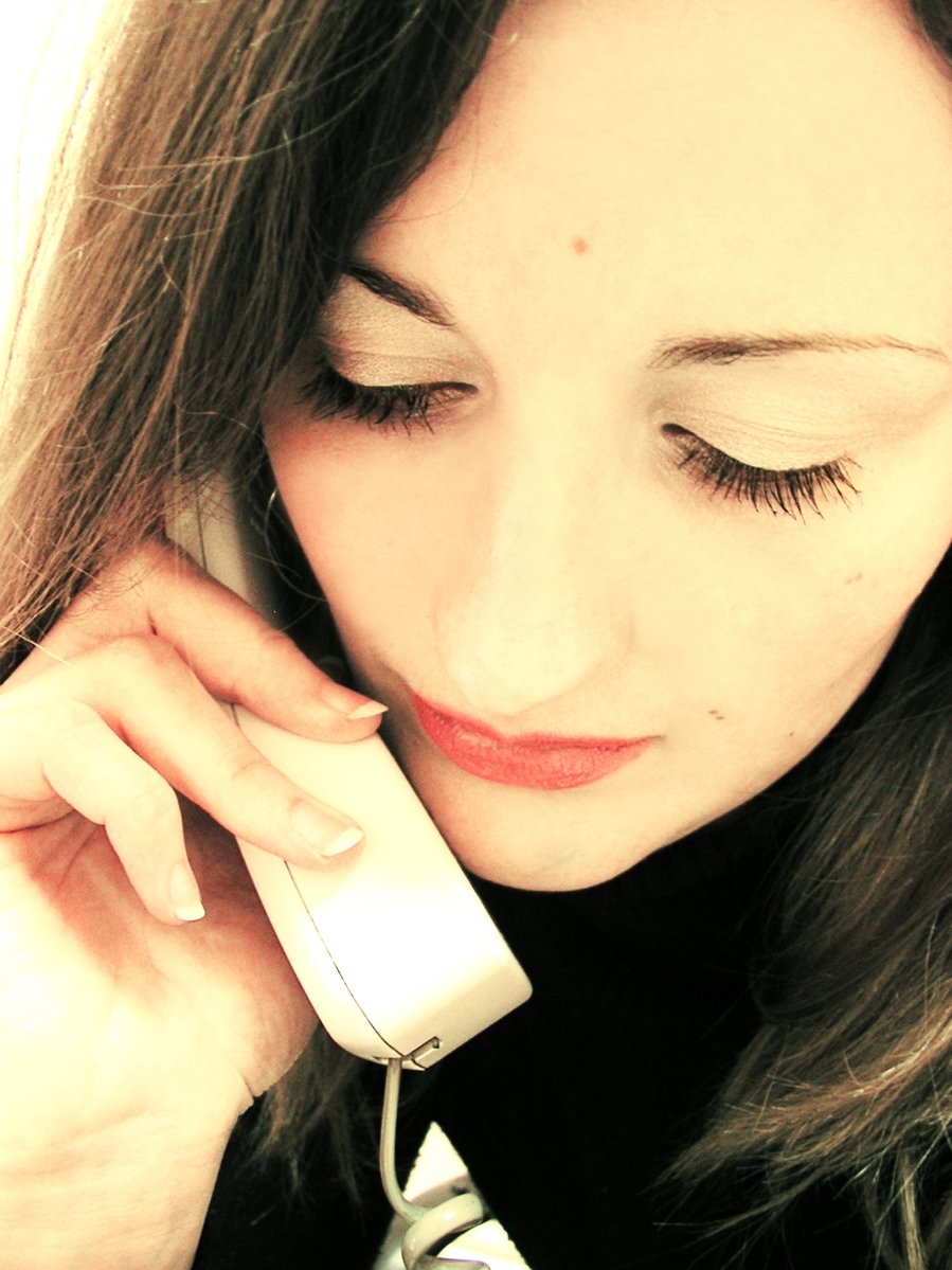 a woman talking on a white telephone and holding a mouse