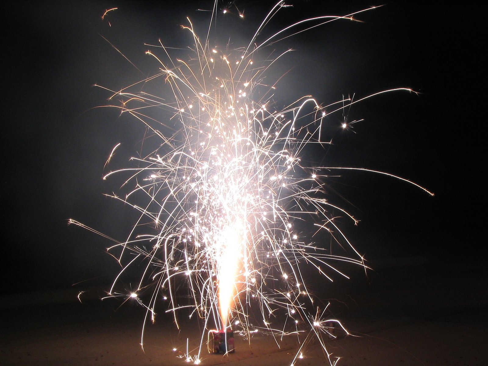 fireworks coming out from a lit up bottle on a beach