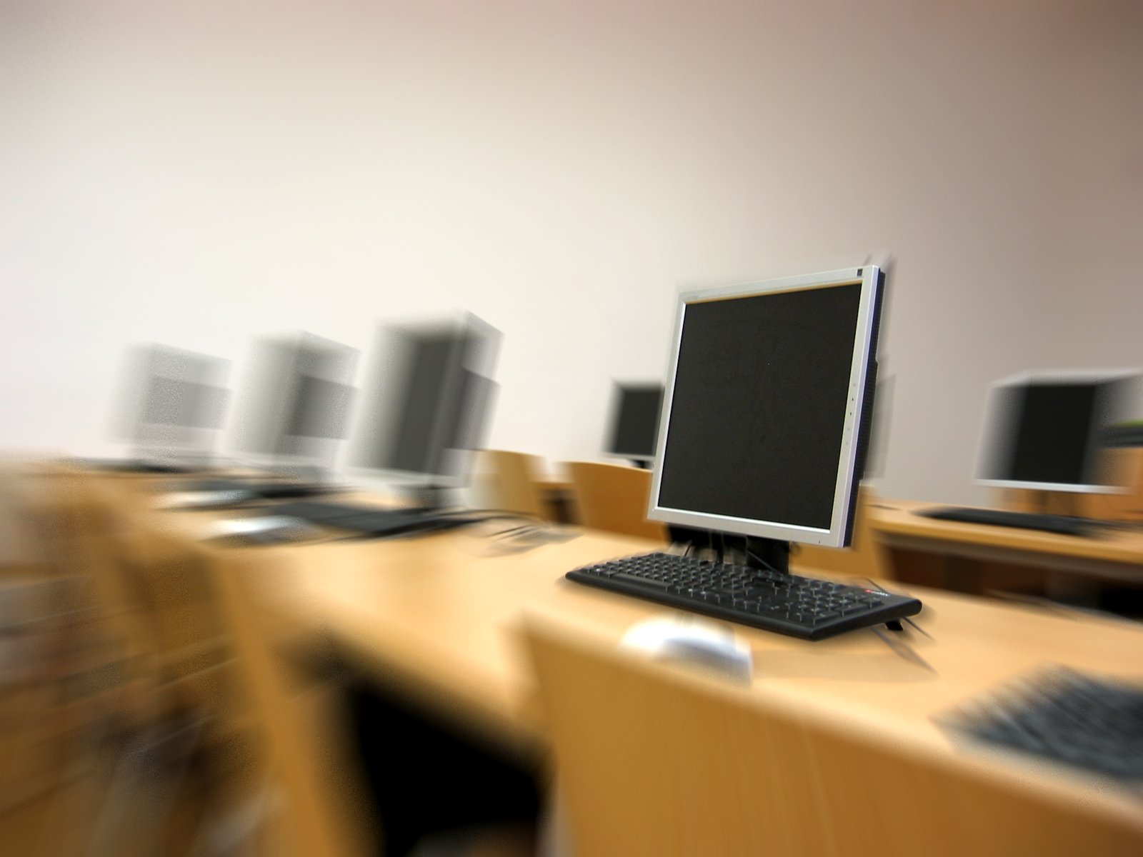 computer equipment on top of wooden desks in a classroom