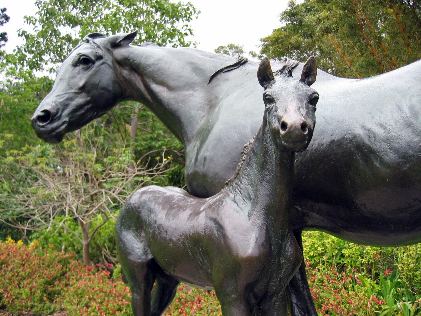 the statue depicts a mother horse and her foal in a garden