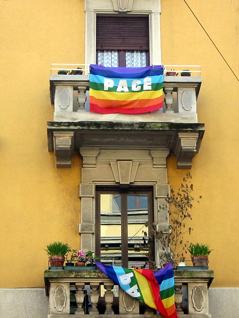a rainbow flag sitting in a window and a big house with an ad for peace written above the windows