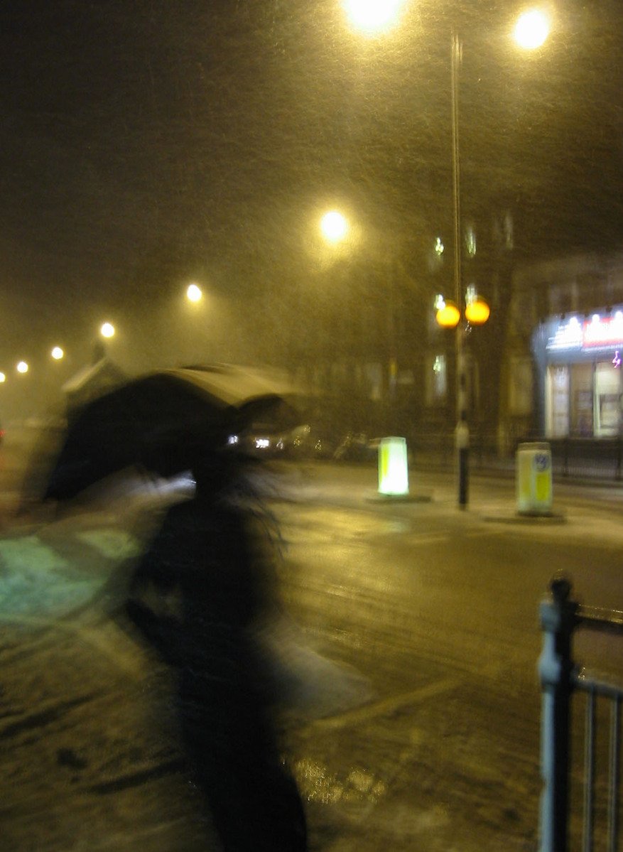 a blurry image shows someone walking down a street with an umbrella
