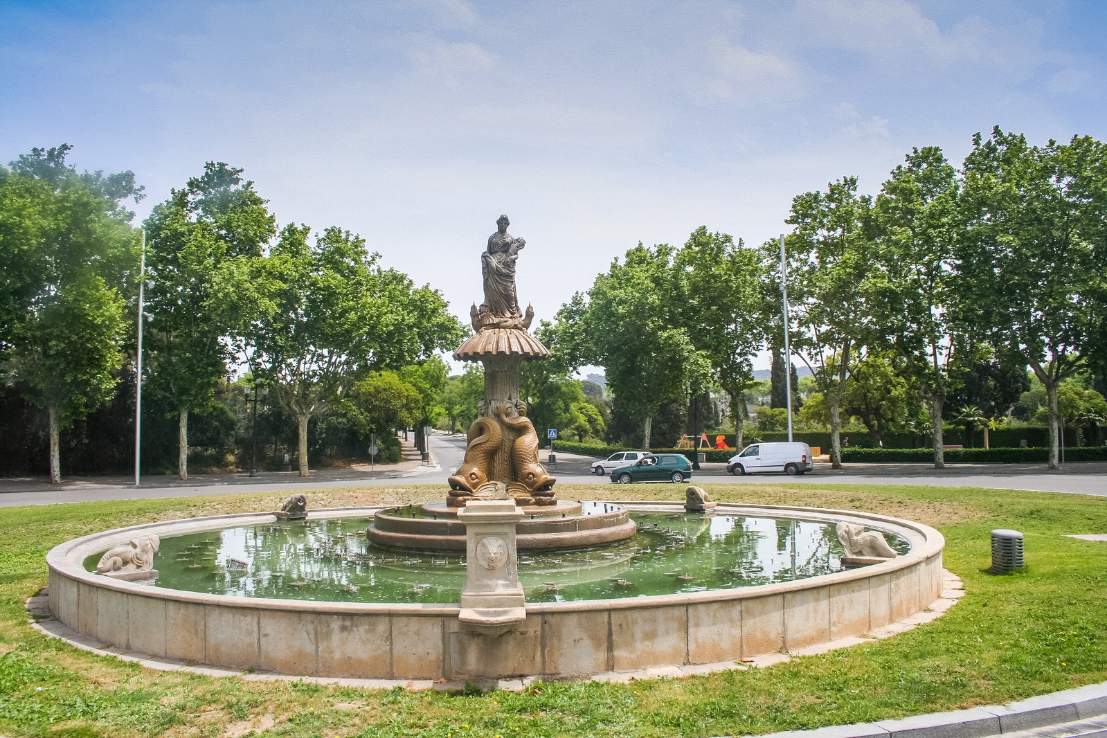 a small fountain with statues sits in the center of a park