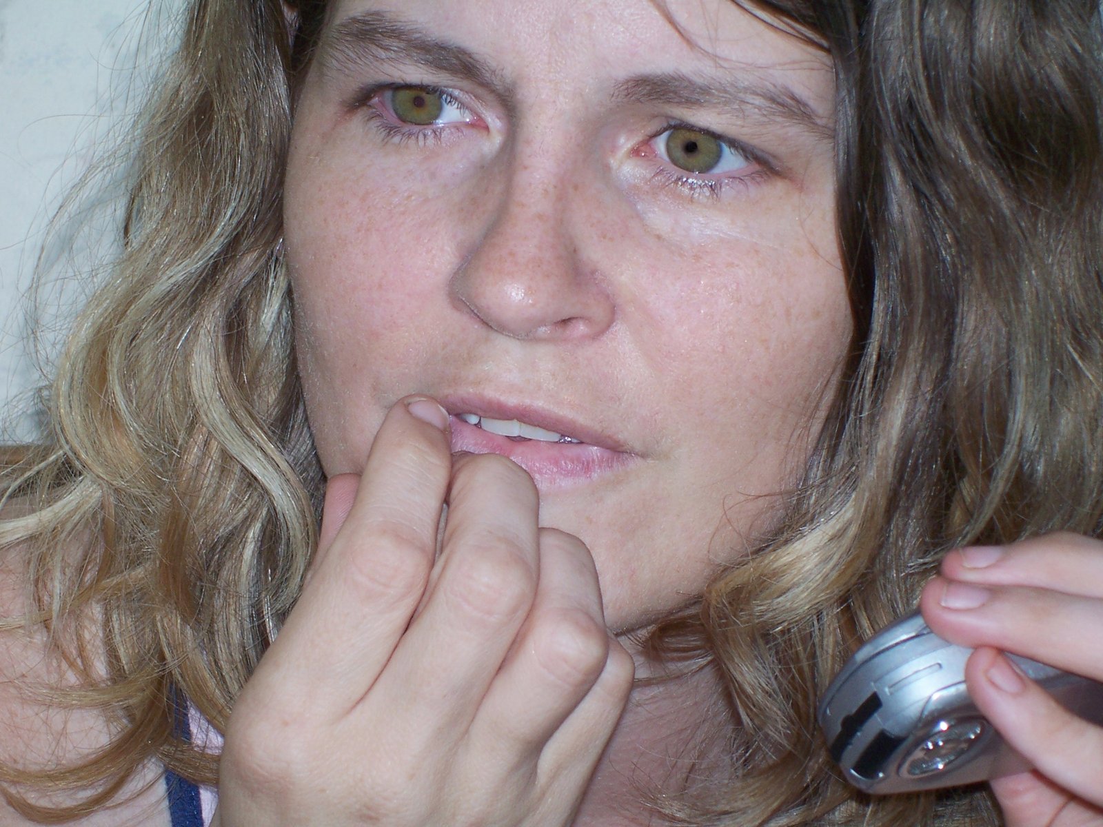 a woman in blue tank top touching her nose with her cellphone