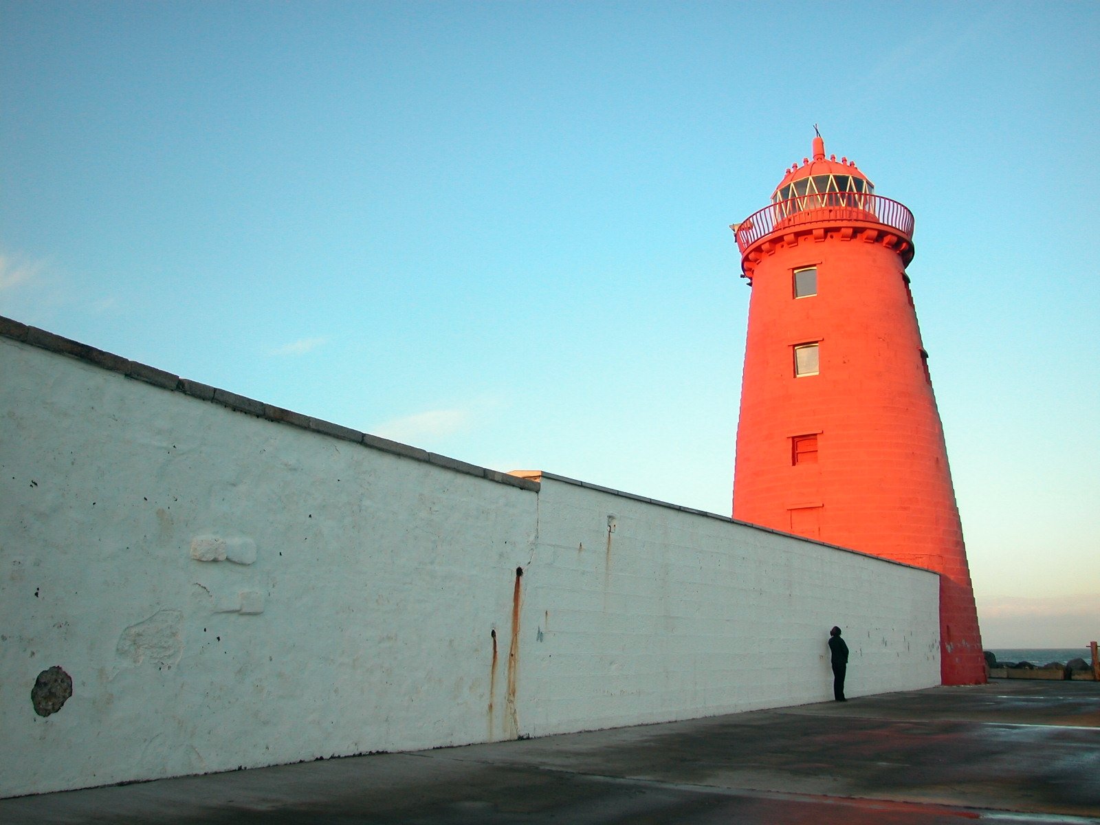 a lone man in front of a white wall and red lighthouse